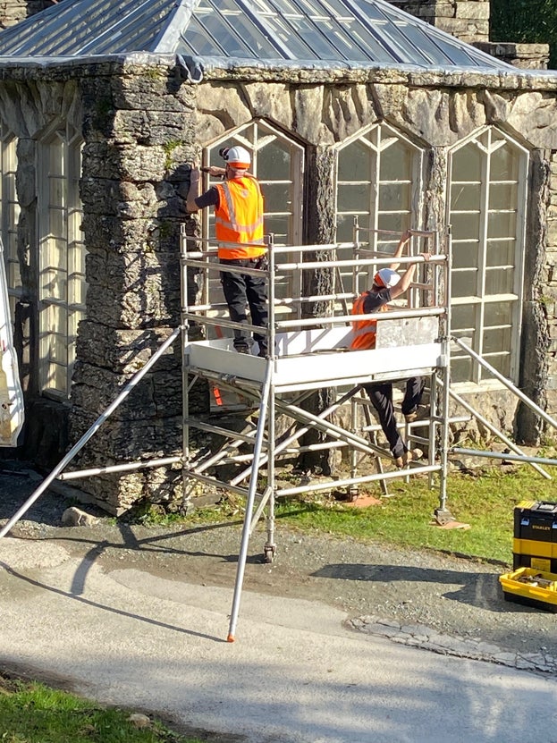 Image of stone built Victorian glasshouse with two people in high vis working on the window restoration